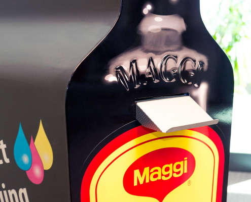 Ausgabeschacht der individuell bedruckten Etiketten aus lebensgroßer Maggi-Würze Flasche