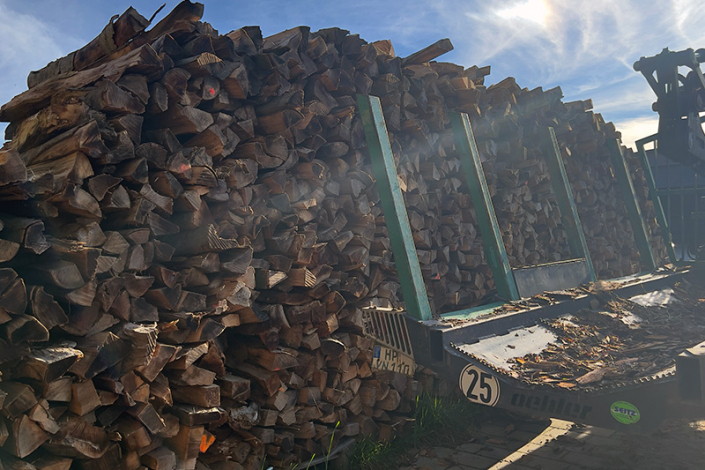 Gestapeltes Brennholz aus eigenem Wald mit Holztransporter davor